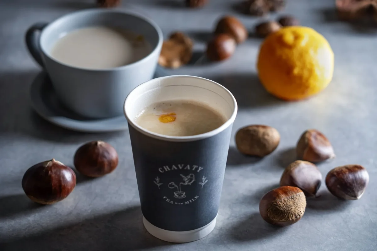 温かい飲み物と栗のクローズアップ写真。カップに入った飲み物、栗、レモンがテーブルに置かれている。