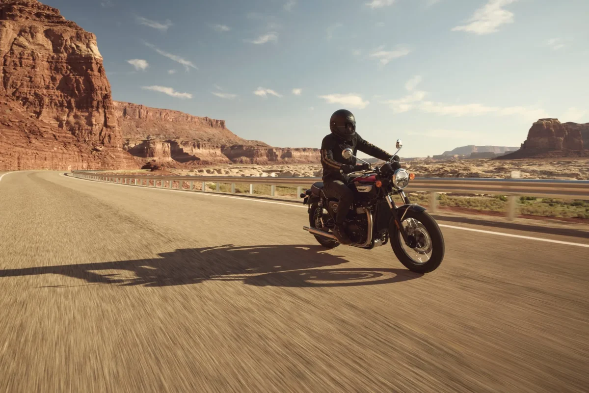 Triumphのバイクに乗って道路を走る人、背景は砂漠