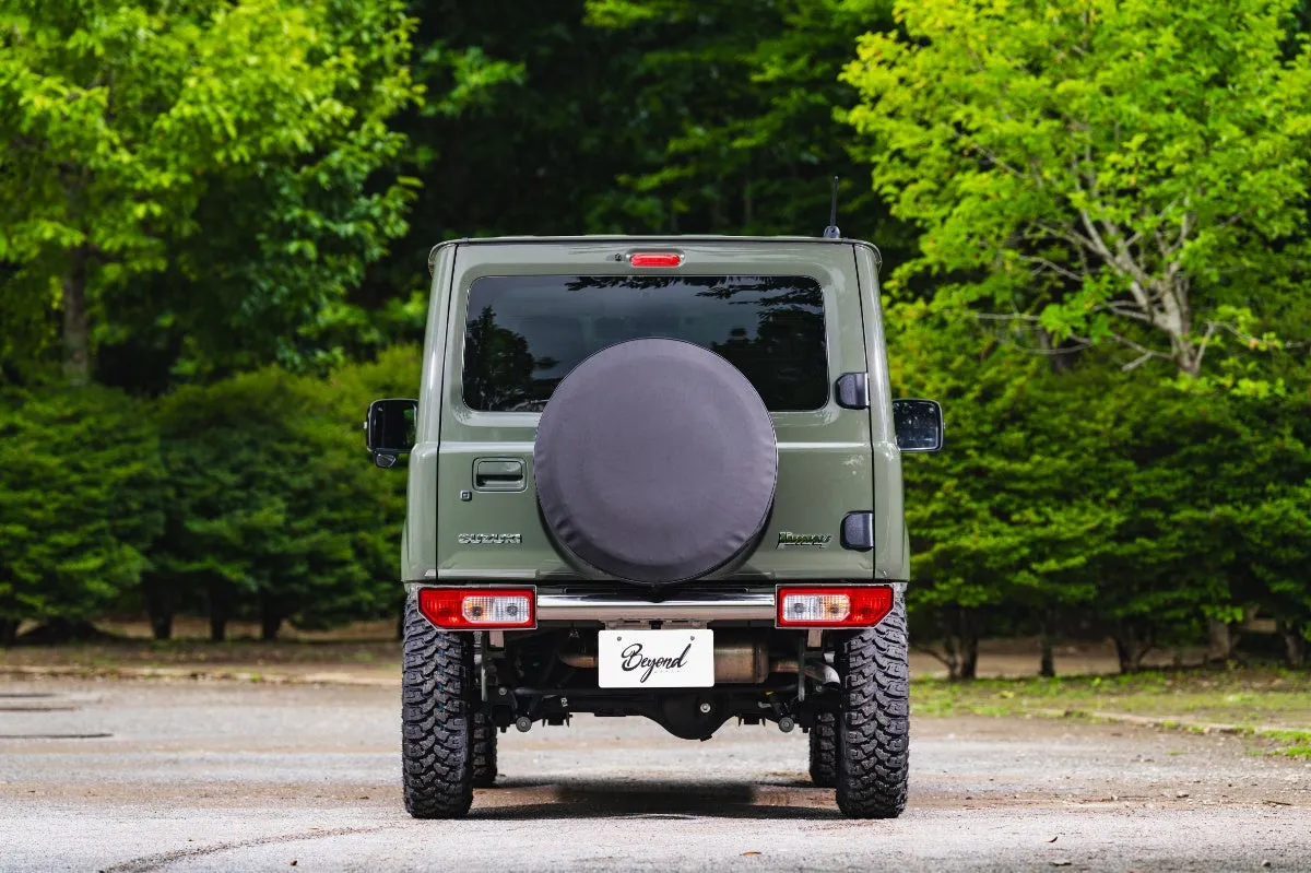 緑色のジムニーの後ろ姿。タイヤが大きく、スペアタイヤが付いている。背景には緑豊かな木々が見える。