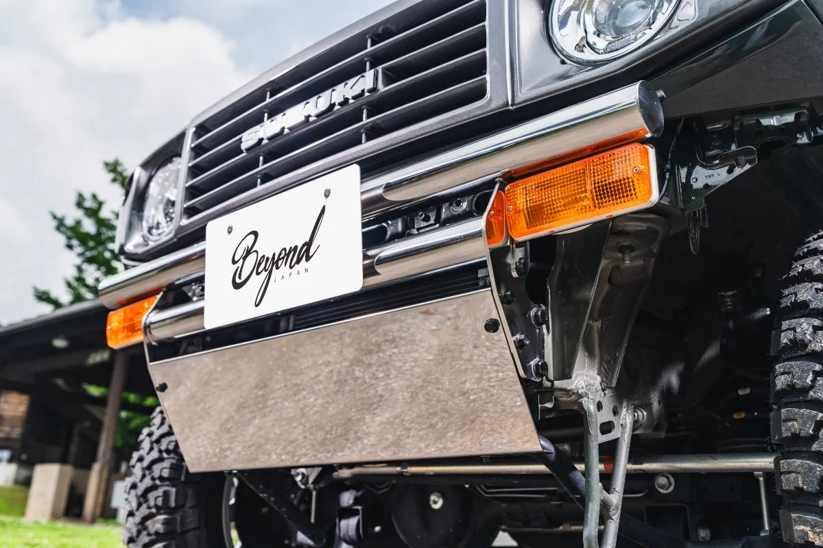 クロムメッキのバンパーとナンバープレート、オレンジ色のウインカーが特徴的なスズキのオフロード車のフロント部分を捉えた写真です。ナンバープレートには「Beyond JAPAN」のロゴが入っています。