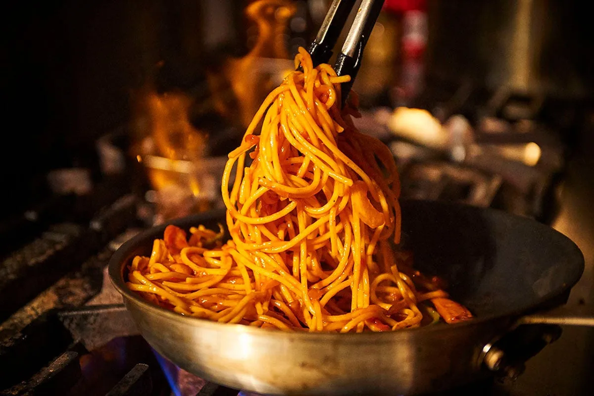 スパゲッティがフライパンからトングで持ち上げられている様子